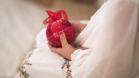 slow motion shot over the shoulder of kid in a christmas white dress holding a red bauble - close up