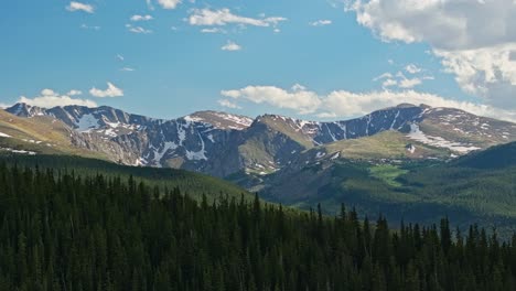 Drone-ascends-evergreen-forest-with-beautiful-snow-left-in-between-dry-barren-mountains