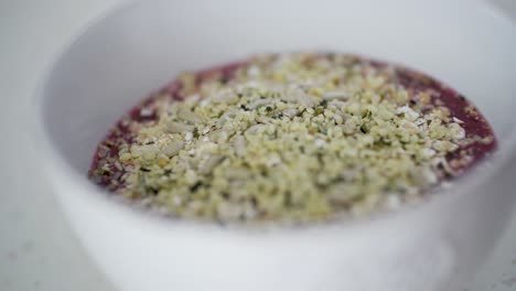 Sprinkling-chia-seeds-on-top-of-red-berry-smoothie-with-oats-in-white-ceramic-bowl