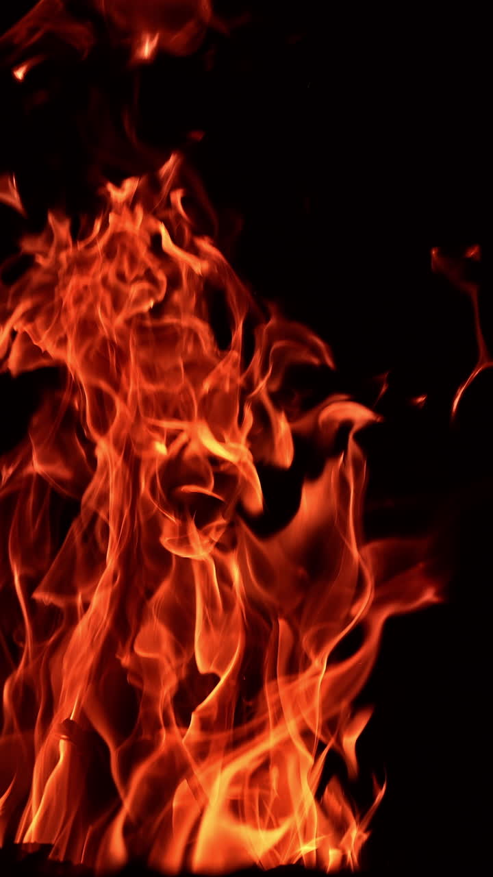 Pieces of wood burning in a big campfire. Large tongues of flame rising up in the darkness. Vertical video