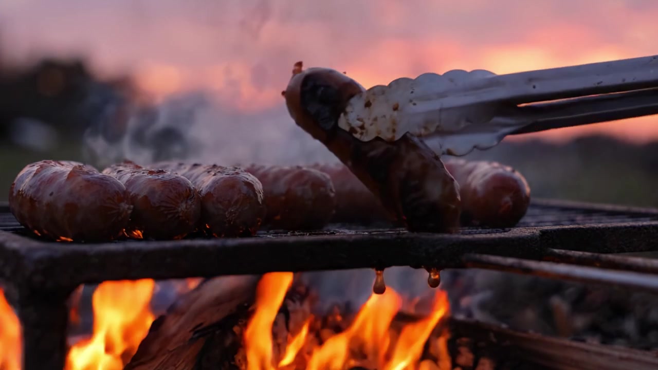 Una deliziosa serata di grigliate: salsicce succulente cotte su fiamma viva con un bellissimo tramonto sullo sfondo che evidenzia l'atmosfera fumosa.