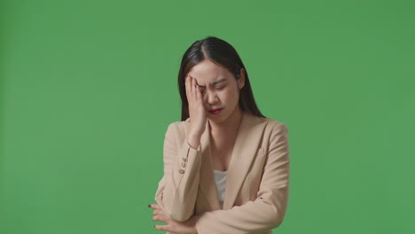 an asian business woman having headache while standing in front of green screen