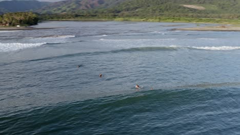 Surfers-catching-waves-off-Pacific-Coast-at-sunset,-aerial-view