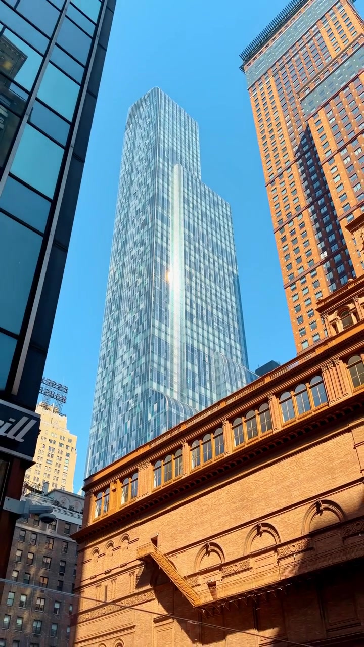 Arranha-céu moderno de vidro erguendo-se acima do histórico Carnegie Hall em Nova York. Vista vertical em ângulo baixo de um arranha-céu de vidro azul e da fachada de tijolos vermelhos do Carnegie Hall em Manhattan