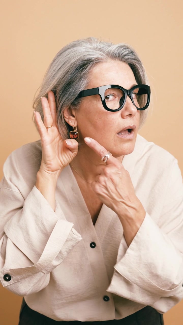 Donna matura con capelli grigi che si porta la mano all'orecchio per ascoltare con attenzione.