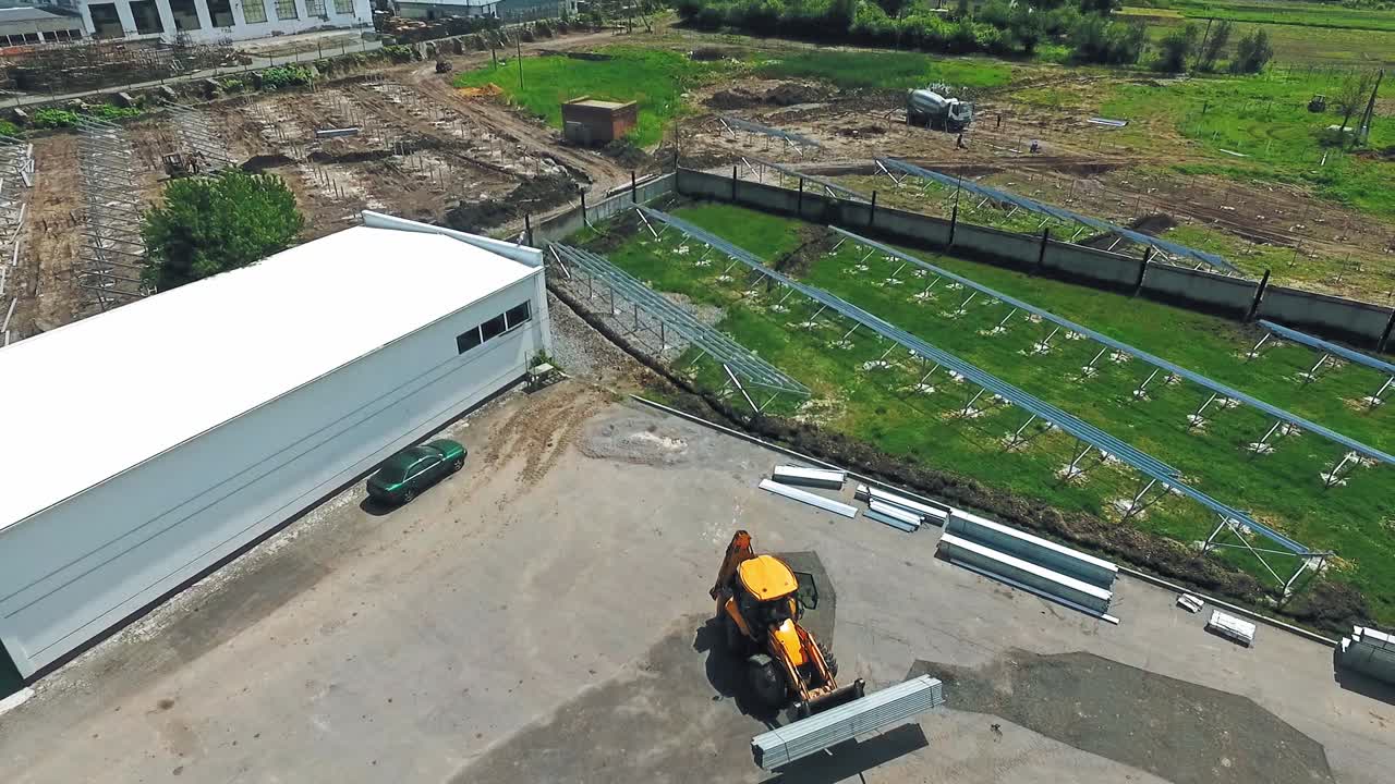 Tractor working on the yard. Industrial machine is carrying cargo on the background of the field on a solar plant construction. Aerial view.