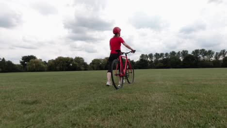 Kaukasische-Radfahrerin-Im-Roten-Oberteil,-Die-Mit-Ihrem-Fahrrad-In-Einem-Park-Geht