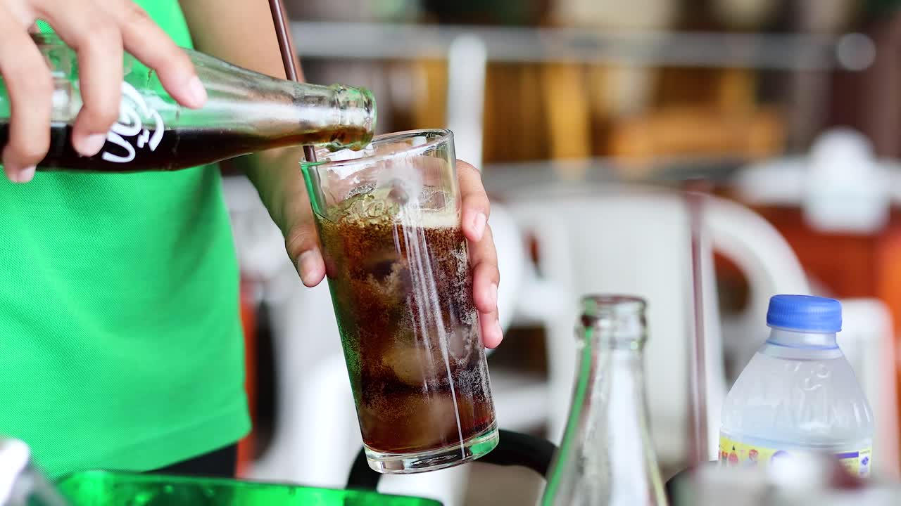 Cola refrescante vertida en un vaso con hielo