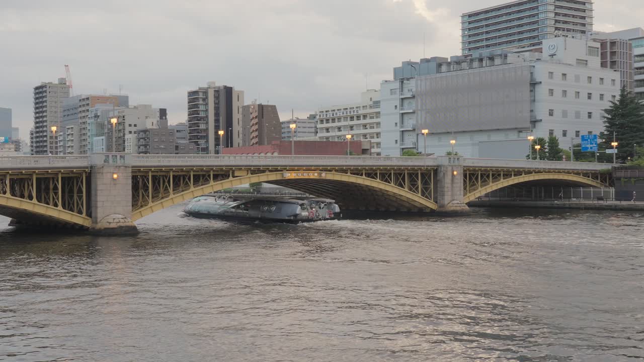 A tourist boat moves down the Sumida River at dusk with Kuramae Bridge in the background