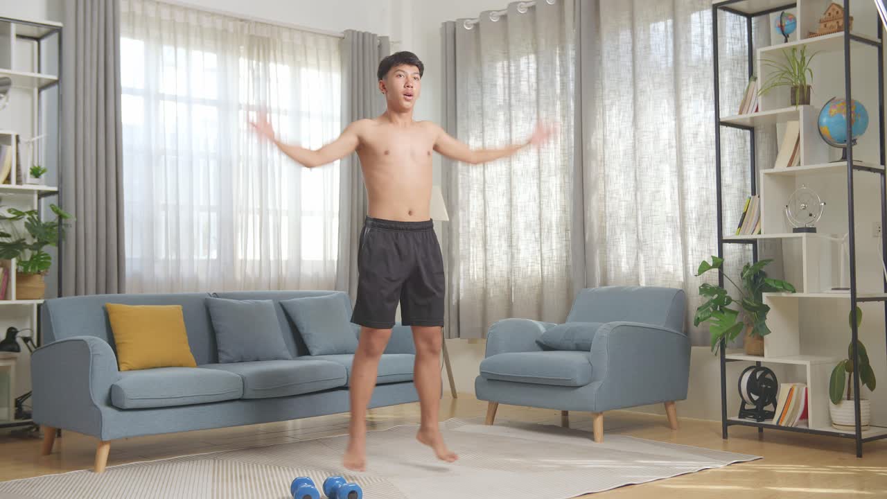 집에서 셔츠를 벗고 운동하는 동안 박수와 함께 점프 잭을 하는 아시아 십대 소년의 몸이 가득 차 있습니다.
