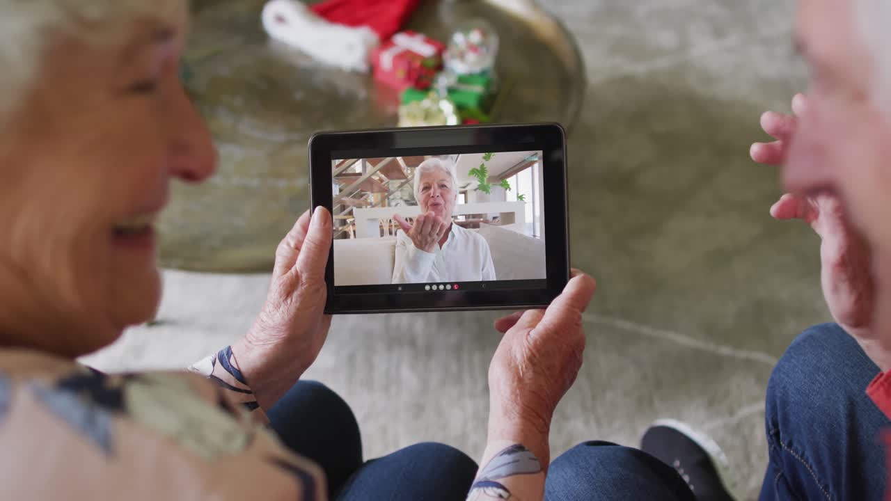 Coppia anziana caucasica sorridente che usa un tablet per una videochiamata di Natale con una donna sullo schermo