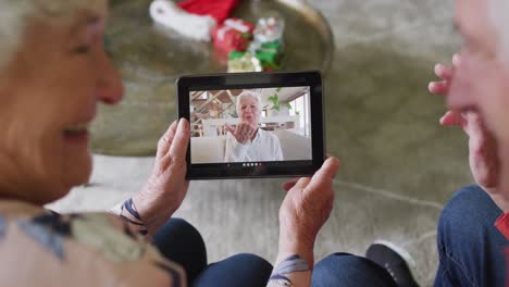 Senior-caucasian-couple-smiling-and-using-tablet-for-christmas-video-call-with-woman-on-screen