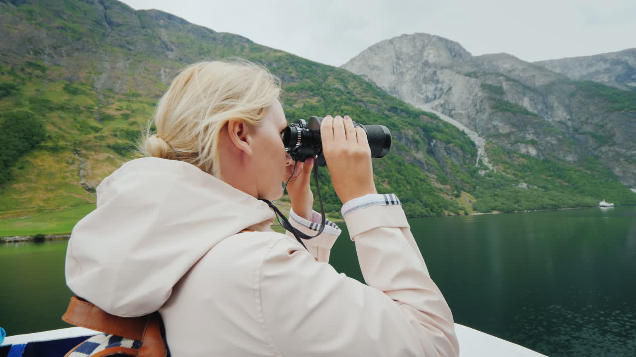 una mujer está de pie en la proa del barco mirando a través de binoculares crucero por los fiordos de noruega