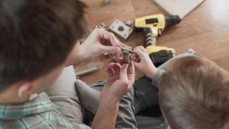 man opens fastening loop and closes it, son shows thumbs up gesture.