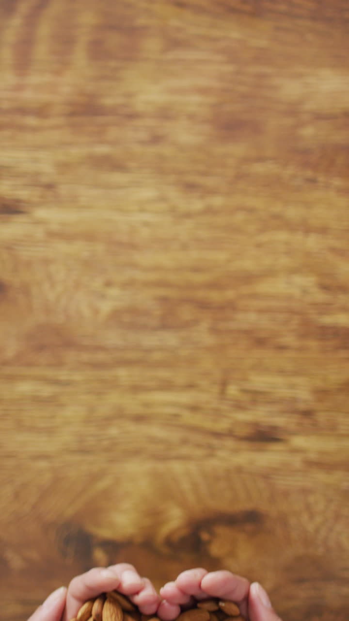 video vertical de manos sosteniendo almendras en forma de corazón sobre un fondo de madera