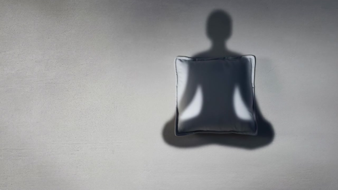 Square reflective pillow remains centered as soft illumination creates bright side highlights and a dark head-and-shoulders silhouette, with subtle shadow movement across a minimal gray setting.