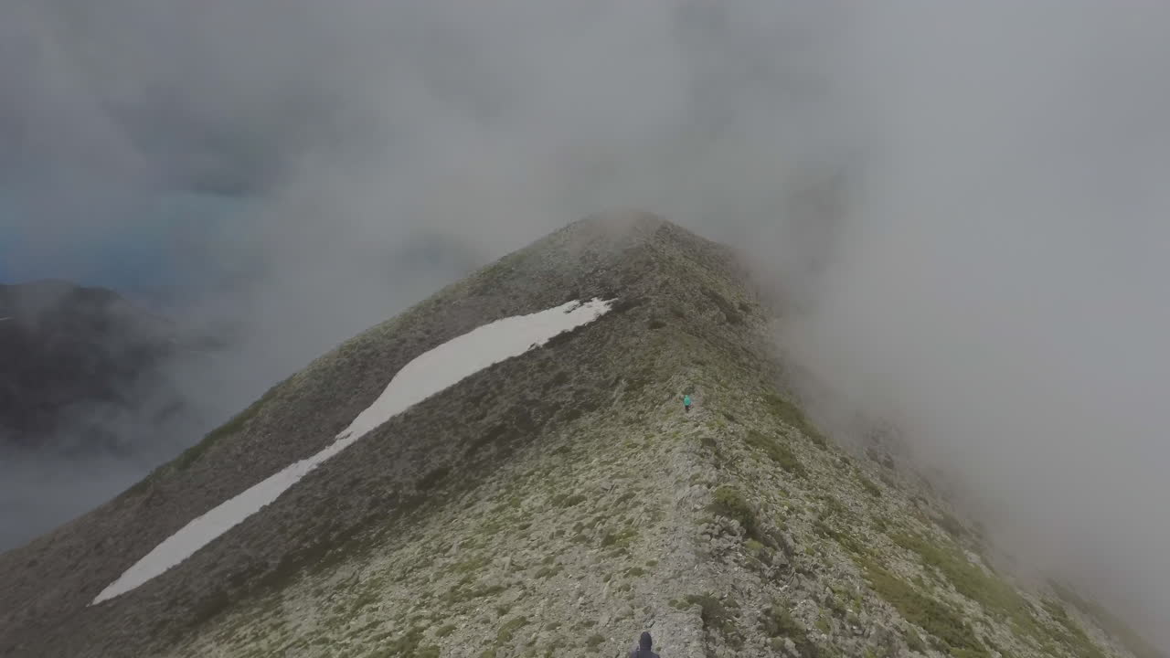Aerial view of a hike woman and man that walk on a mountain peak during a foggy day. Hiker on the top of mountain and drone reveals the landscape. Travel and freedom concept in 4k
