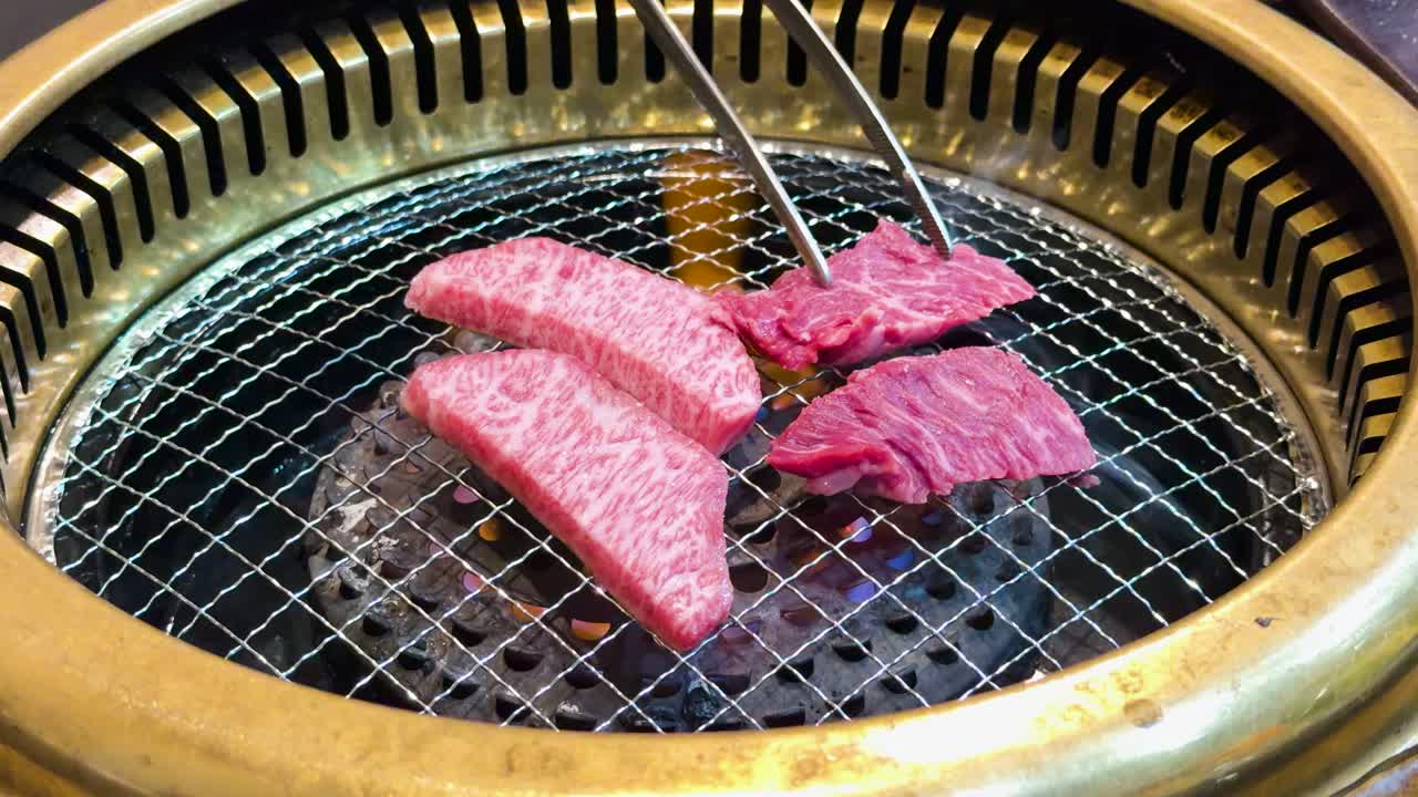 Primo piano di carne di manzo marmorizzata che cuoce su una griglia a carbone con le pinze a Kyoto