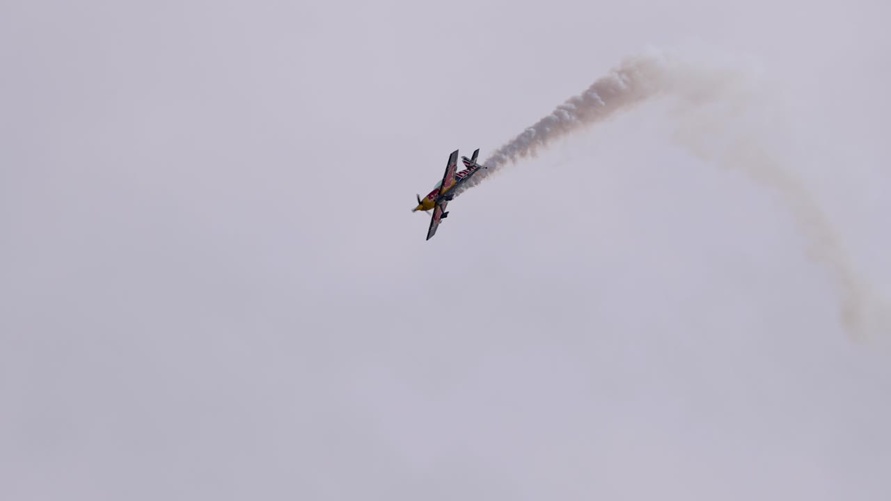 Aerobatic plane executes dynamic maneuvers in cloudy sky, leaving dramatic smoke trails. Captured in a six-second sequence