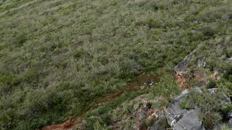 Female-rock-climber-ascending-rock-face,-aerial-reveal-surrounding-landscape