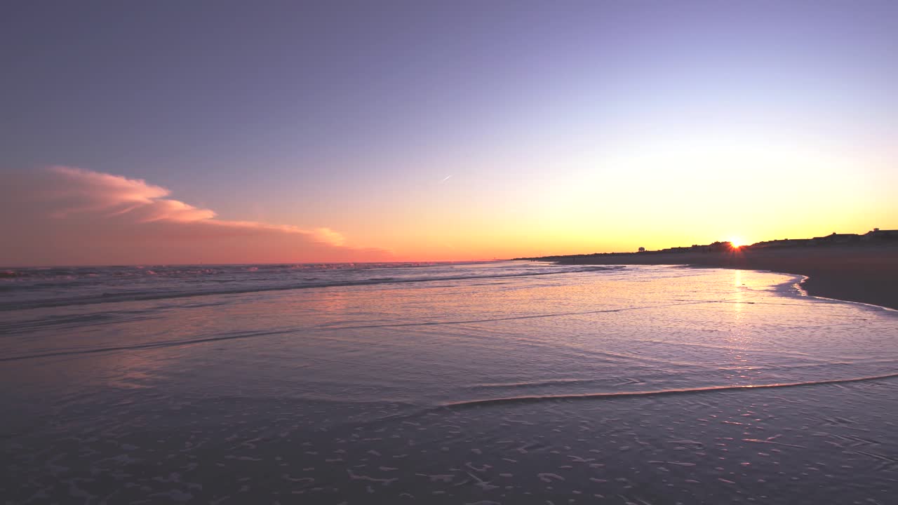 un hombre camina por la playa de arena húmeda tomando fotos con un hermoso fondo de puesta de sol - toma estática