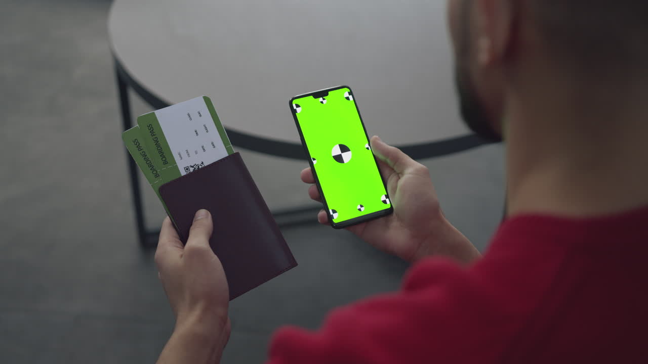 Man Holding Passport, Boarding Passes, and Green Screen Smartphone at Airport