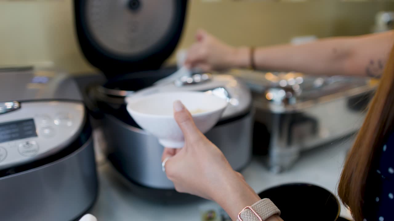 Close-up of hands using a plastic ladle to serve rice from a cooker at breakfast