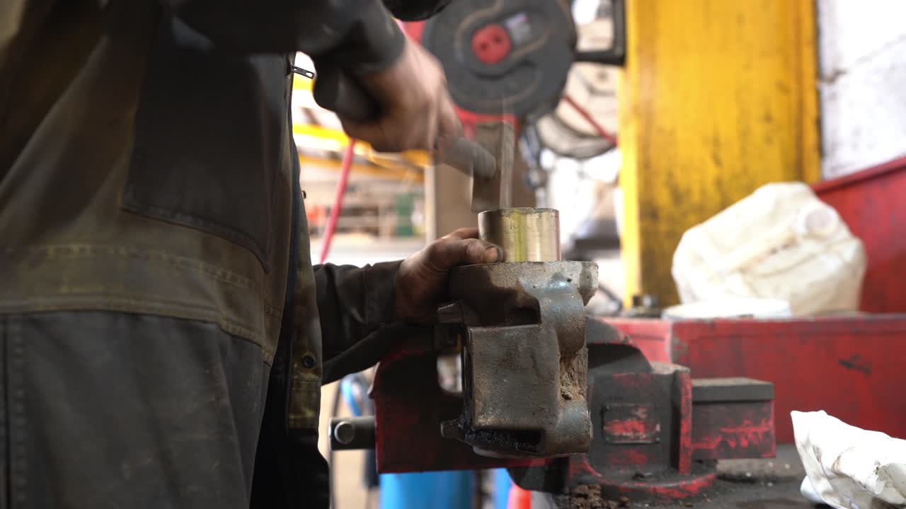A mechanic with very dirty hands hammering home a brass bush into a housing from a commercial vehicle held tightly in an engineer's vice