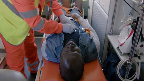 paramédico masculino con mascarilla usando estetoscopio en un paciente estadounidense en la ambulancia 1