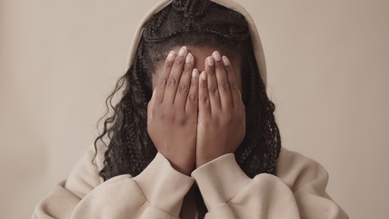 Giovane donna afroamericana che si copre il viso con i palmi delle mani