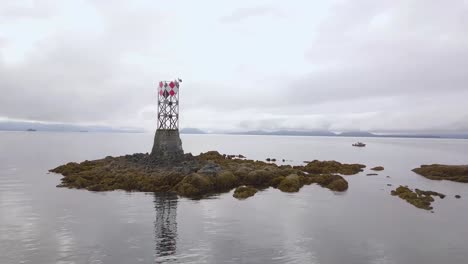 Fast-Aerial-Flyover-Vanderbilt-Reef-with-Navigation-Beacon,-Mountains-and-Diver's-Boat-in-Background,-Juneau-AK,-Lynn-Canal,-Alaskan-Mountain-Range,-Inside-Passage