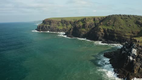 Aerial-pan-left-of-steep-cliff-coastline-with-ocean-waves-crashing