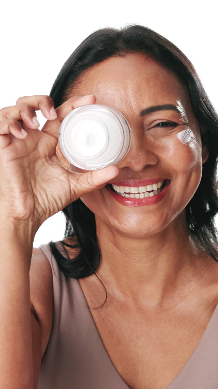 Mujer feliz sosteniendo un tarro de crema para la piel sobre el ojo y sonriendo.