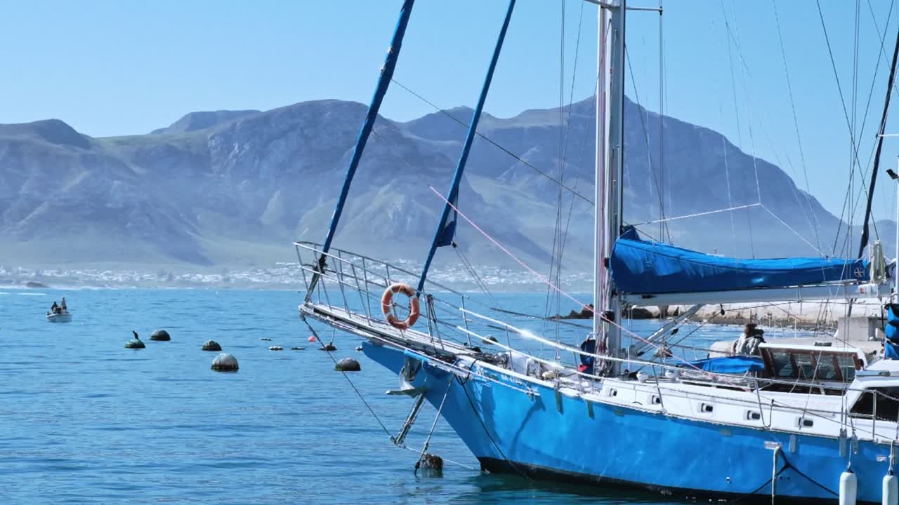 A blue sailing yacht in a harbor on a beautiful calm day with mountains in the distance