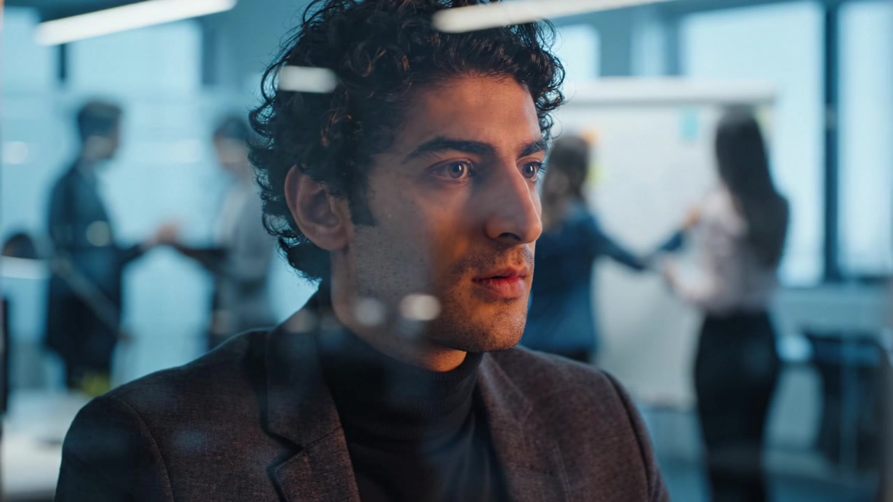 Focused Professional in a Modern Office Setting, Pondering Over Insights While Colleagues Collaborate in the Background During a Strategic Meeting Session