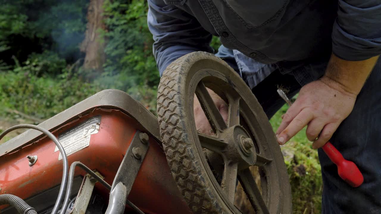 hombre limpiando la rueda de la cortadora de jardín