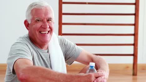 Senior-man-smiling-at-camera-sitting-on-floor