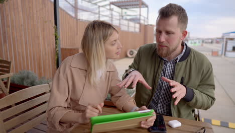 couple discussing work on tablet in outdoor cafe