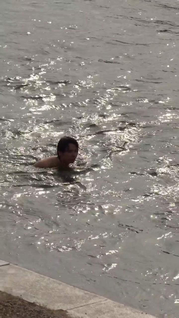 Asian man swims in a sunlit river with shimmering water reflections and natural lighting.