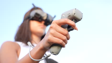 Close-Up-of-Young-Woman-Hand-Holding-Remote-Motion-Controller-With-Goggles-Headset-on-Her-Head,-Selective-Focus,-Low-Angle
