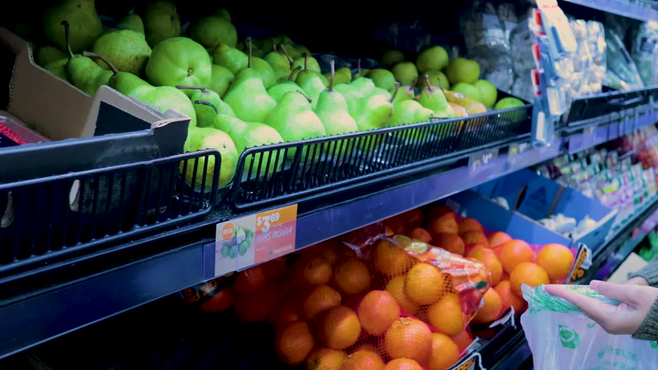 쇼핑객이 멜버른 슈퍼마켓의 활기찬 농산물 전시장에서 신선한 진주를 선택하여 일상적인 식료품 쇼핑을 전시합니다.