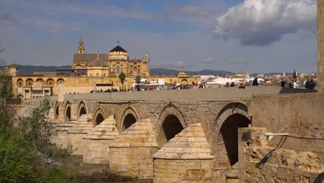 Tourists-walking-over-bridge-in-Cordoba,-Spain-on-clear-sky-day