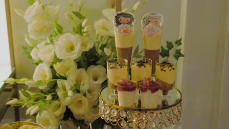 close up shot showing a cake stand with multiple dessert glasses, white flower decorations in the background