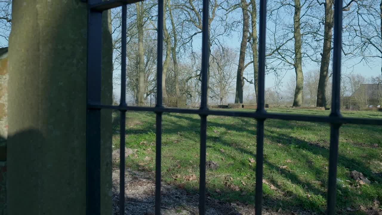Vieja puerta de metal se abre lentamente para revelar un cementerio tranquilo