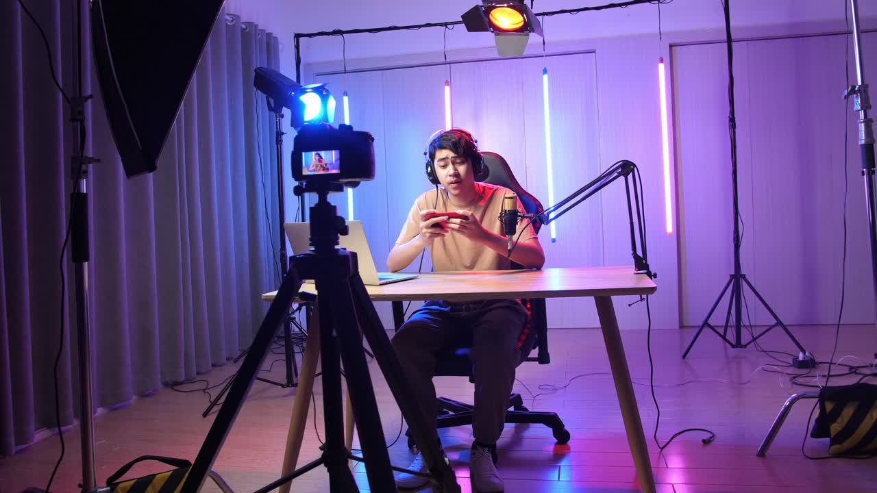 Asian Man Playing Video Game With Mobile Phone Then Pose And Smiles To Camera While Live Stream, Professional Light Equipment