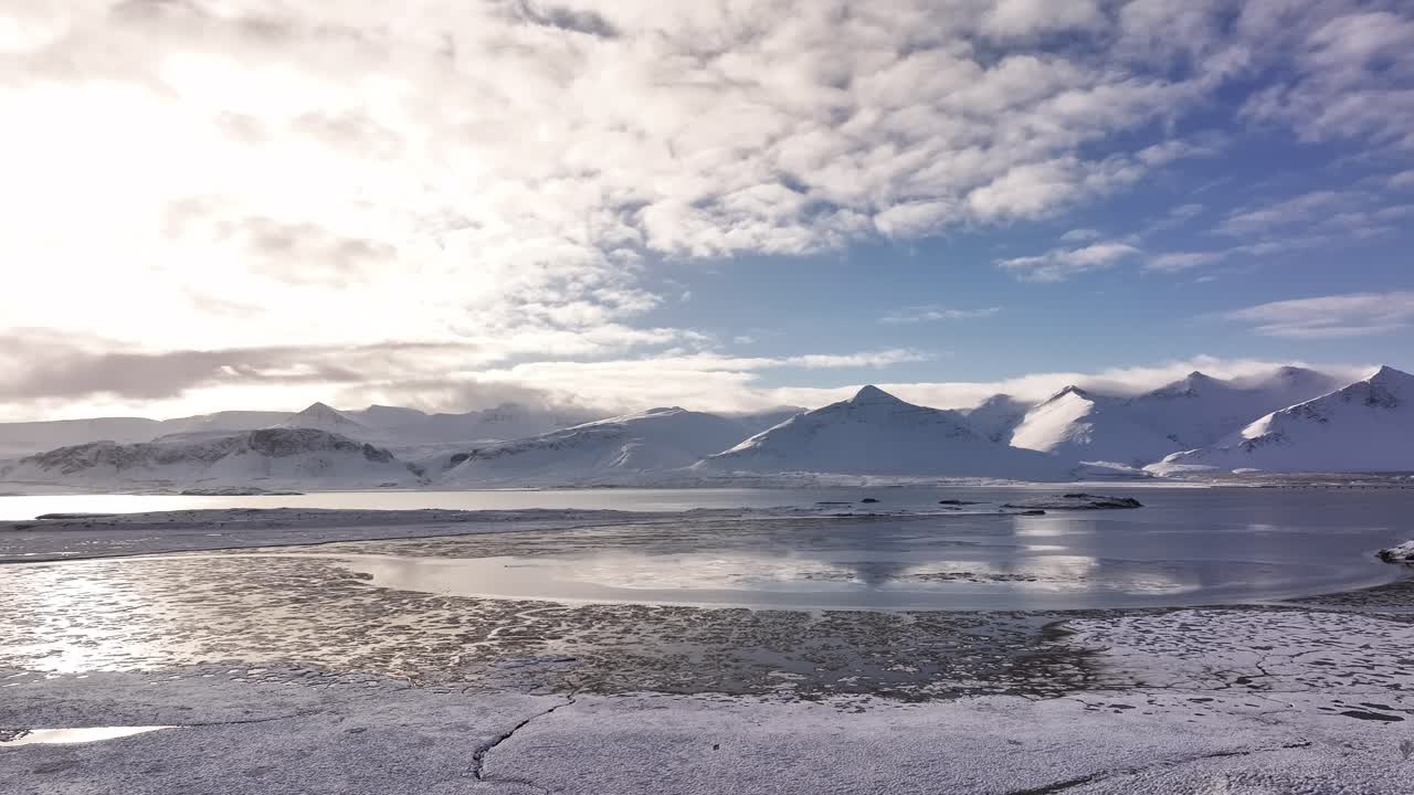 Snow-covered mountains and a partially frozen lake under morning light near Borgarfjörður, Iceland.