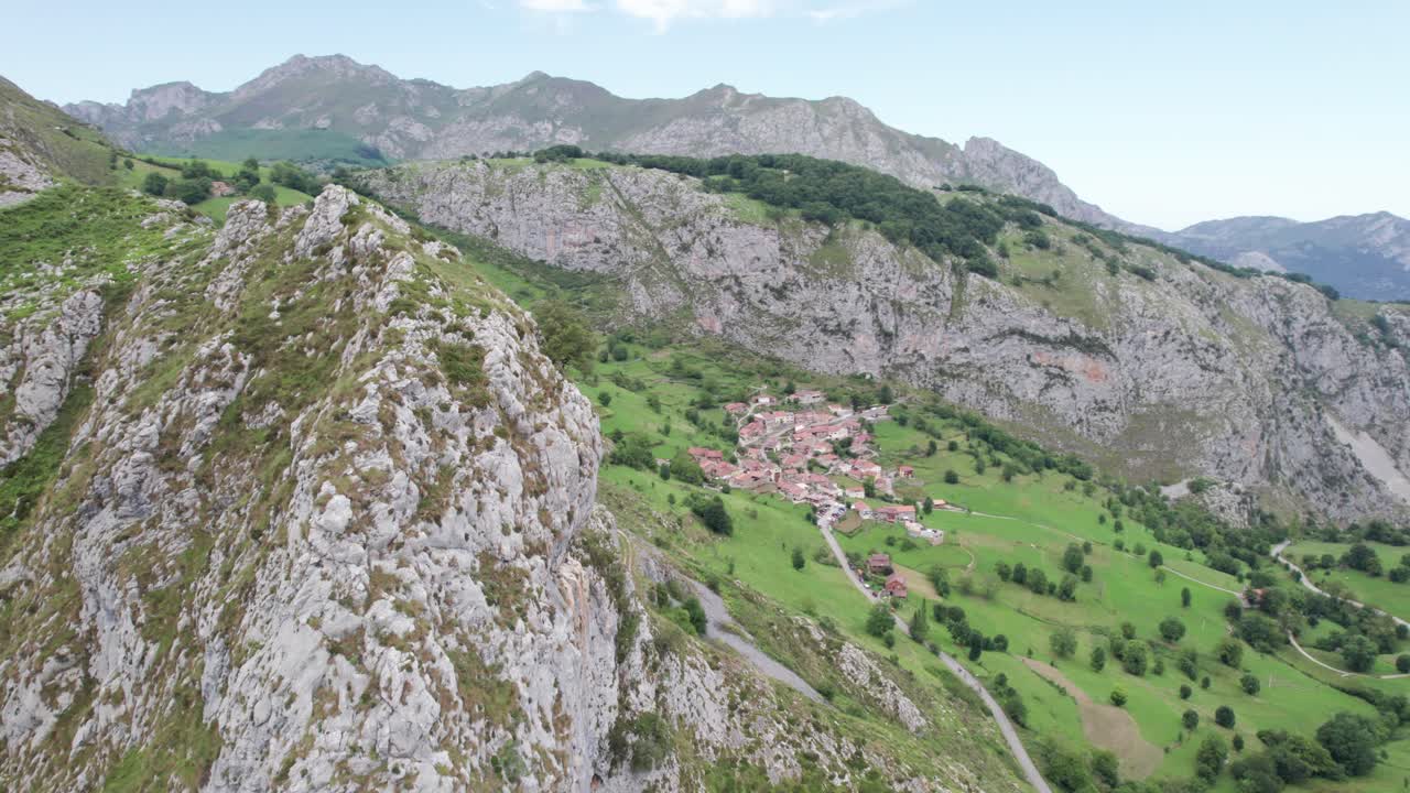 enormes laderas de montañas grises empinadas que apenas están cubiertas de vegetación con un hermoso pueblo histórico español en valles pasiegos en un día soleado