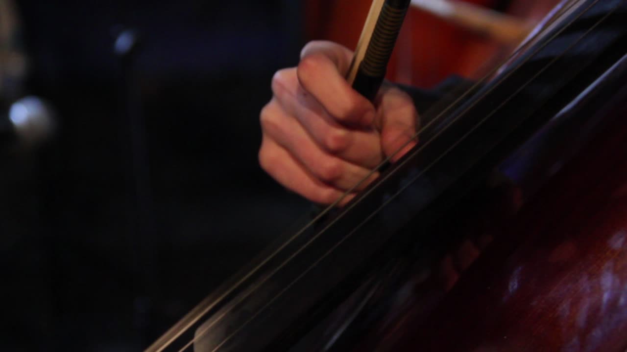 Primo piano di una mano che suona il violoncello con l'archetto.