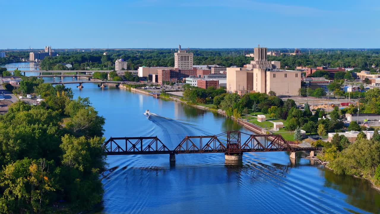 Fiume Saginaw con una barca che passa sotto un ponte ferroviario, edifici della città che costeggiano il lungomare