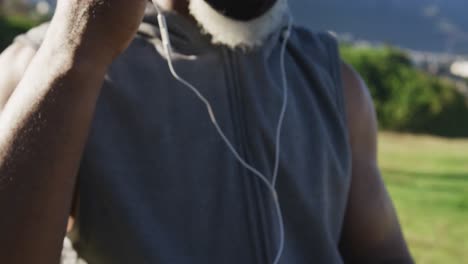 Senior-african-american-man-wearing-face-mask-exercising-putting-earphones-in